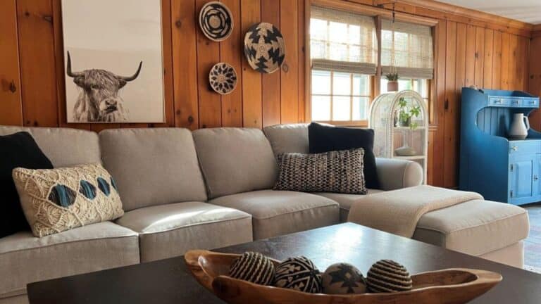 Cozy living room with beige sectional sofa and wooden wall decor, farmhouse style interior, natural light, decorative pillows, boho accents, creating a warm and inviting home ambiance.